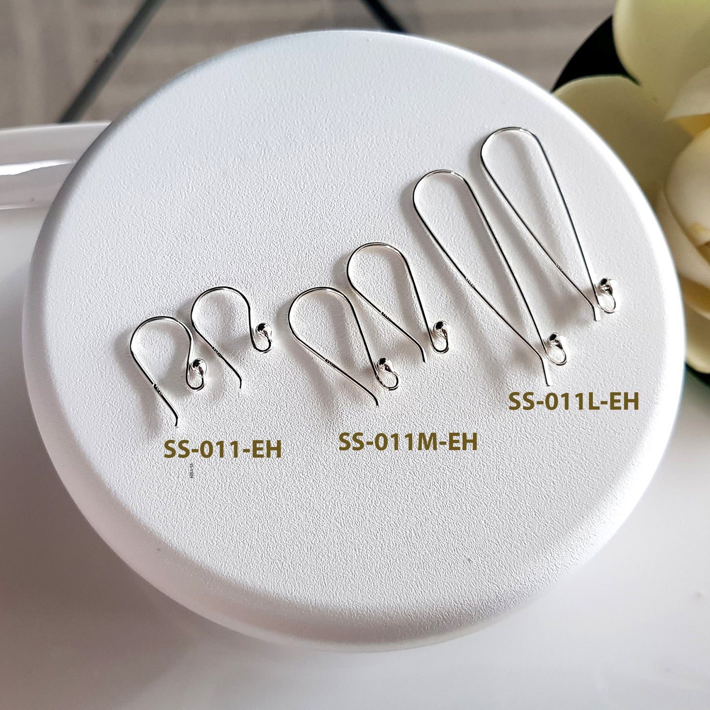 Set of silver earring hooks on a white round tray with labels.