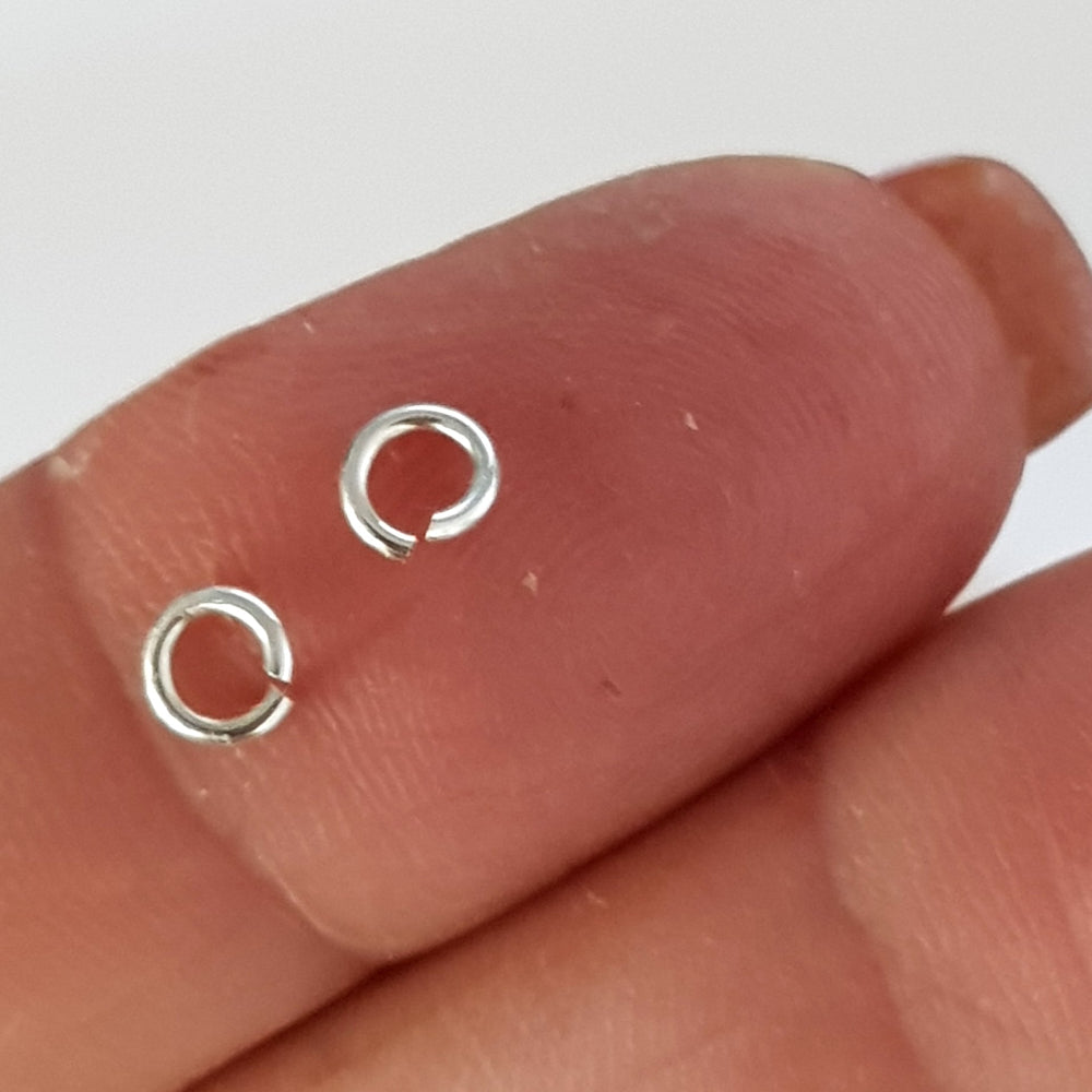 Two silver open jump rings jewellery components held between fingers against a neutral background
