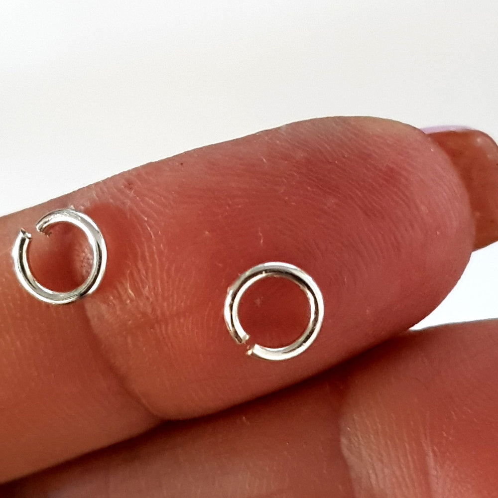 Two silver open jump rings on a person's finger against a white background