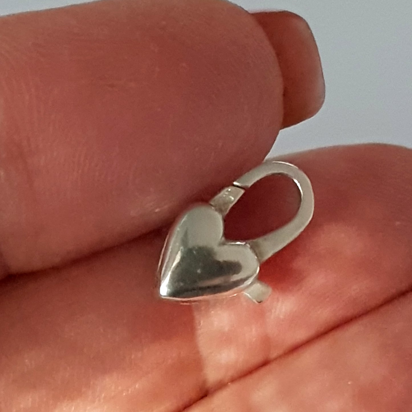 Silver heart-shaped clasp held between fingers against a neutral background