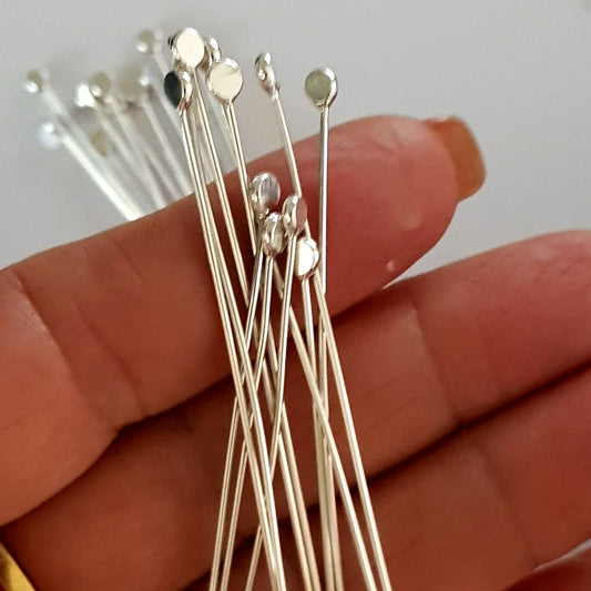 Silver headpins held between fingers against a neutral background
