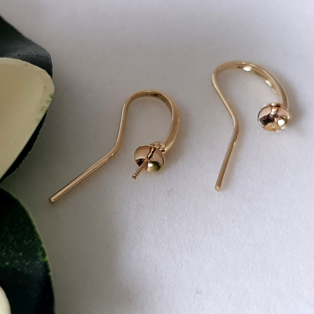 yellow gold earring hooks with pearl cup laying against a white background