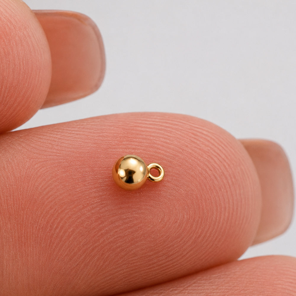 A 14k gold filled 3mm ball drop with jump ring on a finger for size.