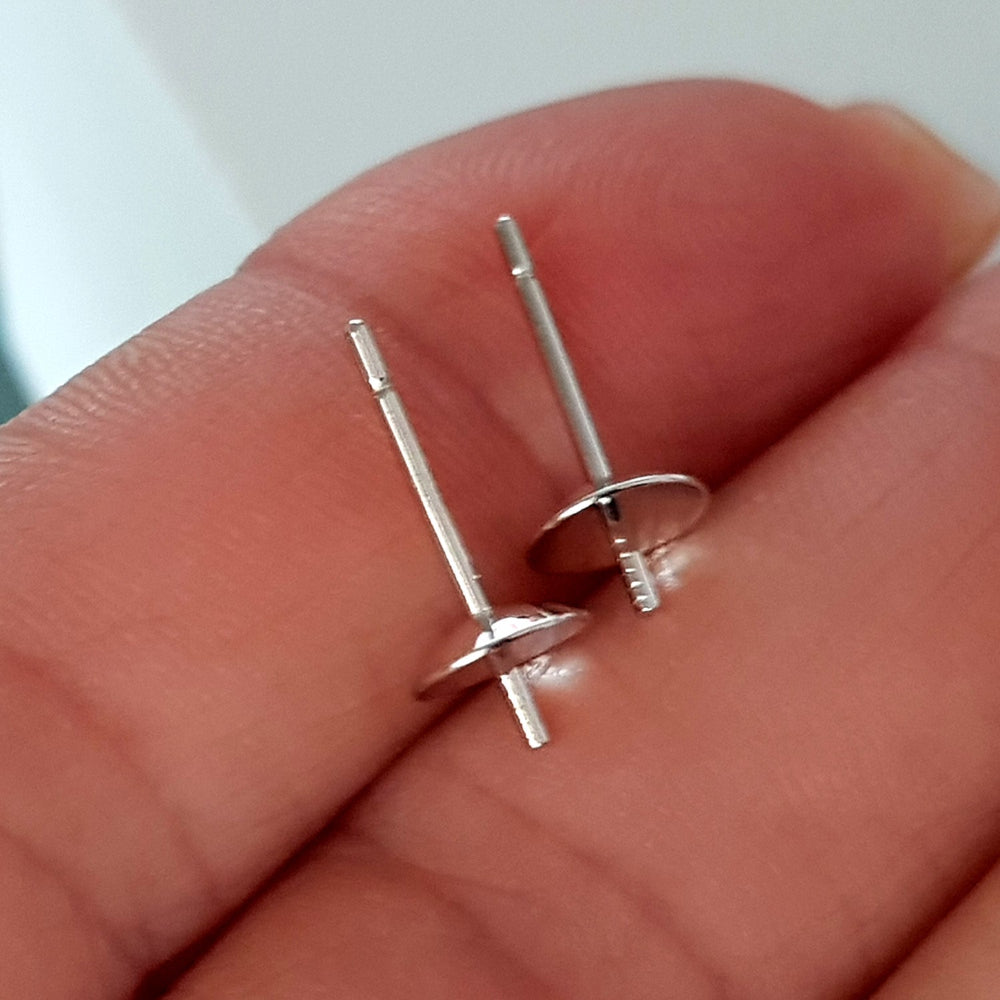 Silver earring studs held between fingers against a neutral background