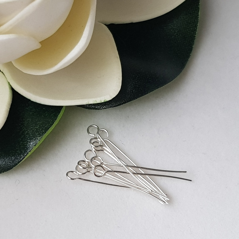 Eye Pins 20mm laying on a white background with a flower on the corner,