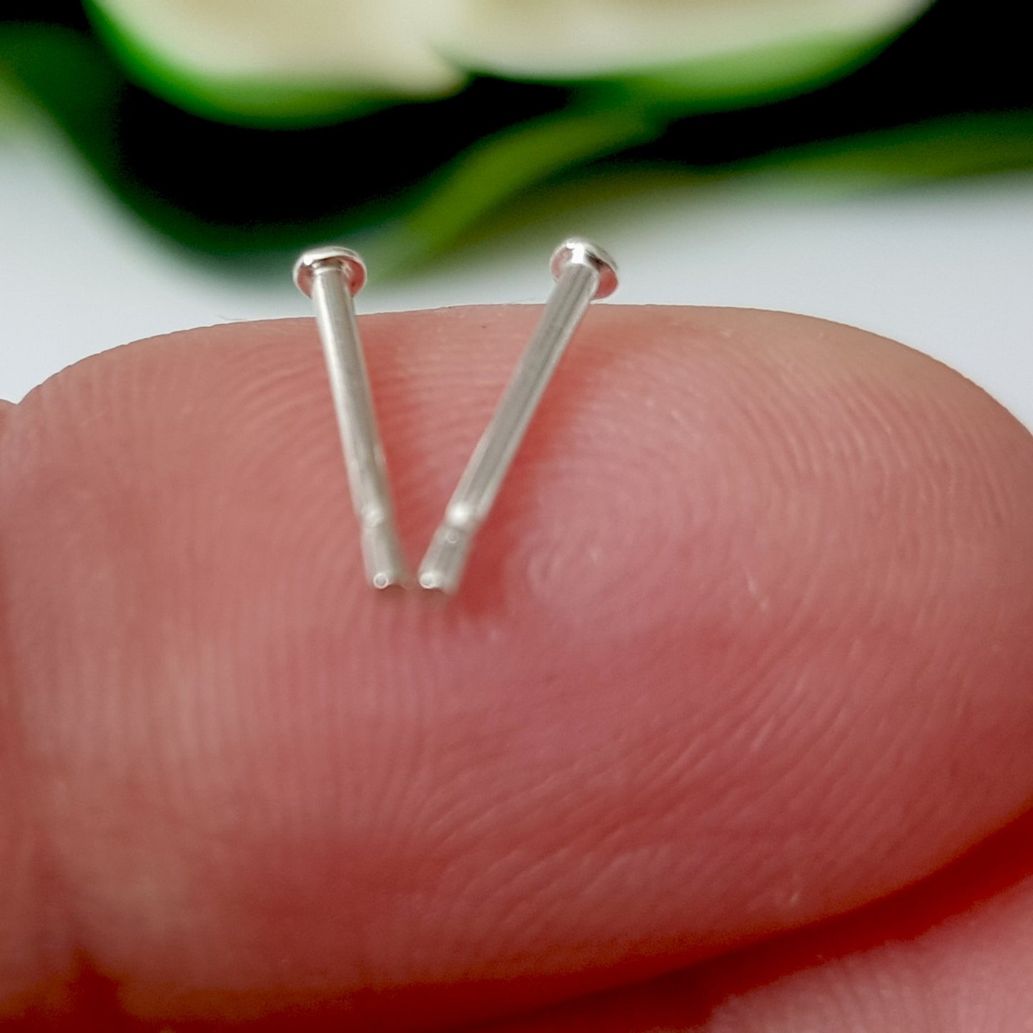 A close-up of a sterling silver earring post with a 2mm disc, held between fingers.