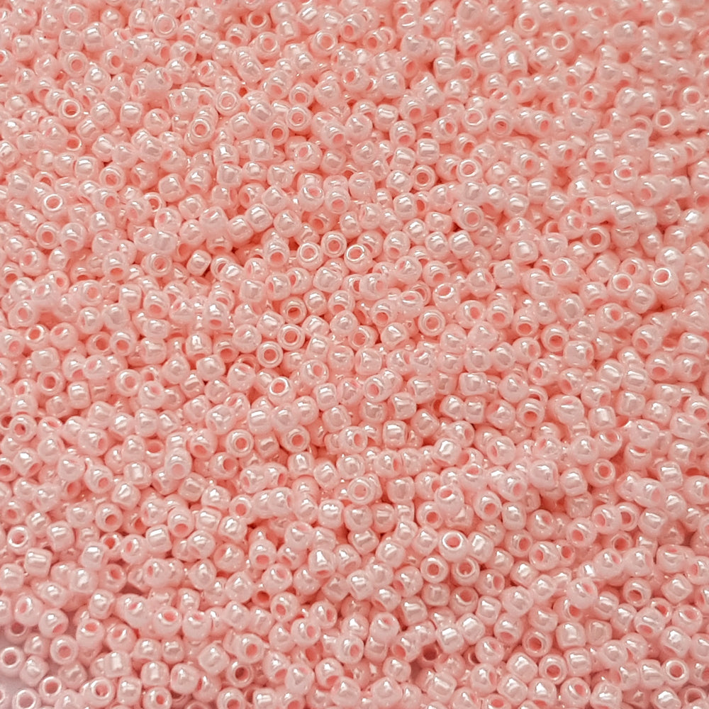 A round container filled with baby pink opaque luster Toho seed beads. close up.