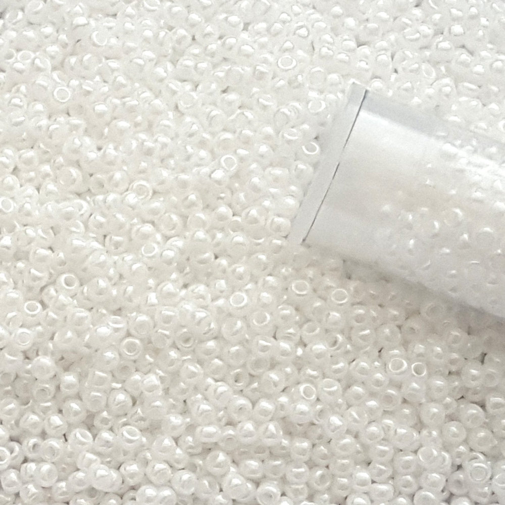 11/0 TR-121 White Opaque Lustre Round Toho Seed Beads close up with the end of a tube.
