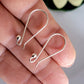 Silver earring hooks held between fingers against a neutral background