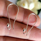 Silver earring hooks held between fingers with a blurred floral background
