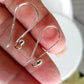 Silver earring hooks held between fingers against a neutral background