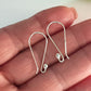 Silver earring hooks on a hand against a neutral background