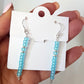 Turquoise beaded earrings on a white card held by a hand.