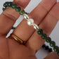 Hand holding a necklace with green beads and a pearl, on a white background