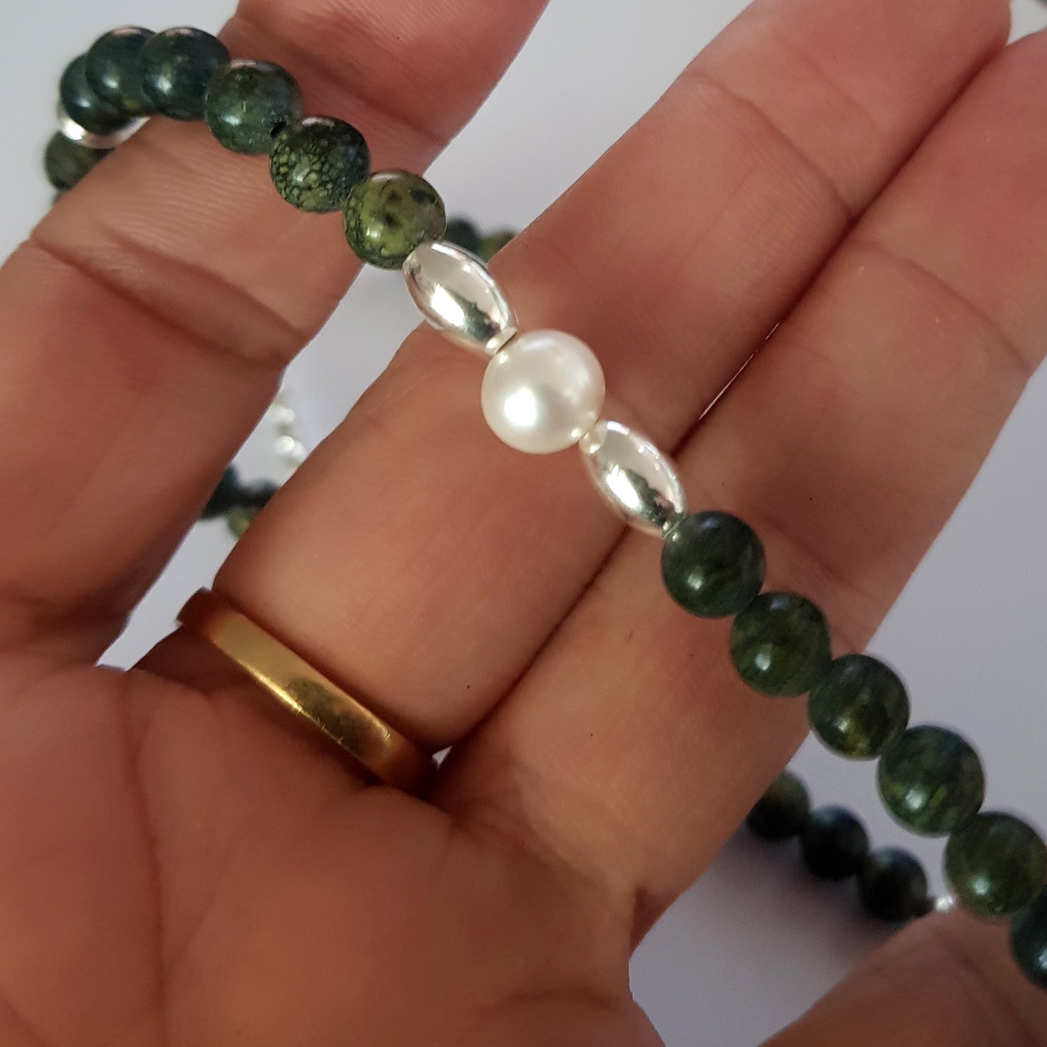 Hand holding a necklace with green beads and a pearl, on a white background