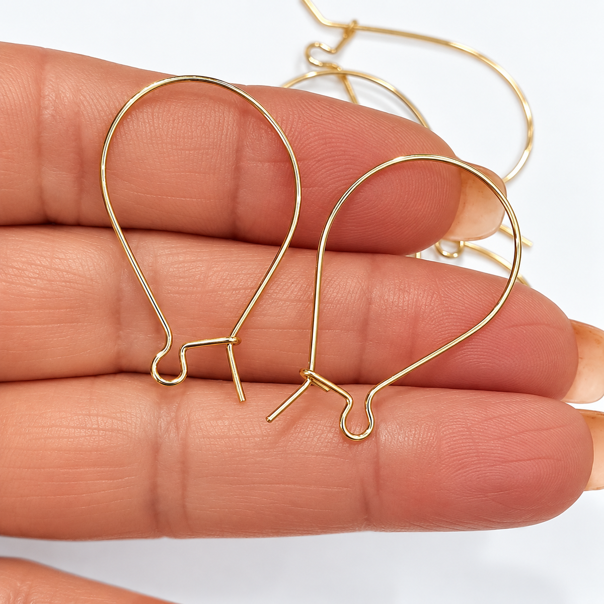 Close-up of two gold filled kidney ear hooks held in hand showing locking closure and 0.7mm wire gauge detail