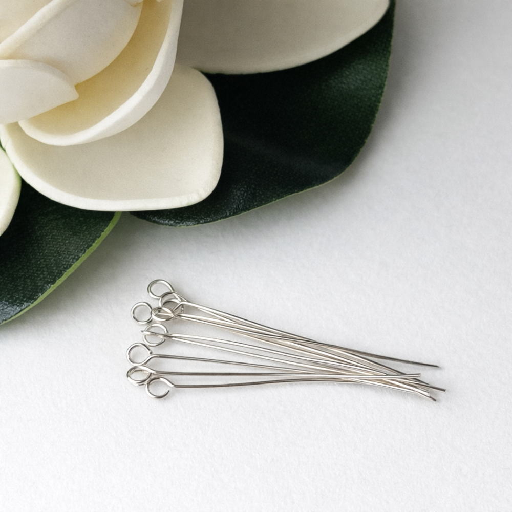 Silver eye pins on a white surface with white flowers and green leaves.