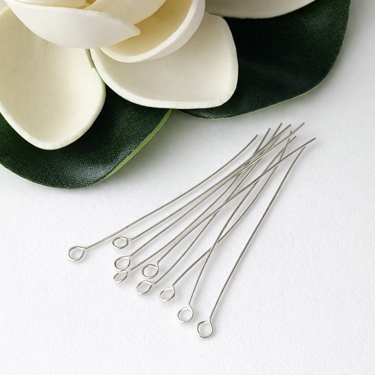 Silver eye pins on a white surface with decorative elements