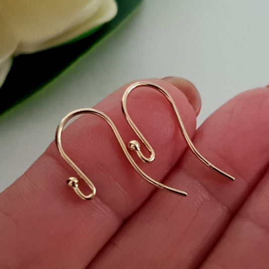 A pair of 9ct yellow gold earring hooks with balled ends displayed on a person's hand.
