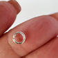 Silver open jump ring on a finger against a white background
