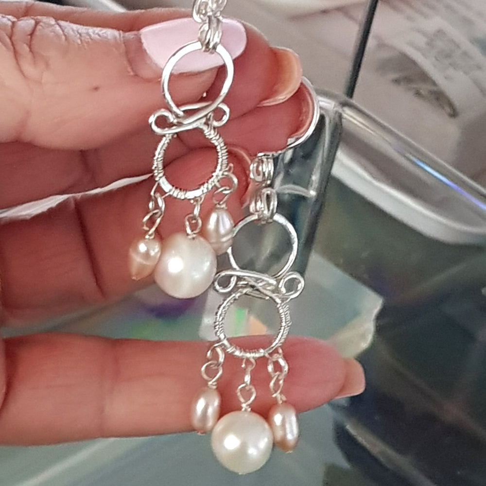Both handmade chandelier pearl earrings held in hand showing the pair together, sterling silver wirework with white and soft-pink freshwater pearls – FKJ-210E by Kalitheo