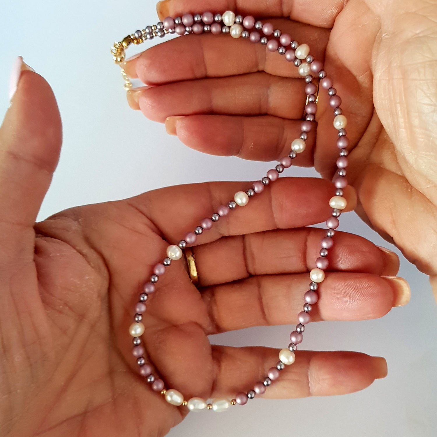 Hand holding a pearl necklace with a light background