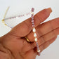 Hand holding a beaded necklace with pearls and pink beads against a white background
