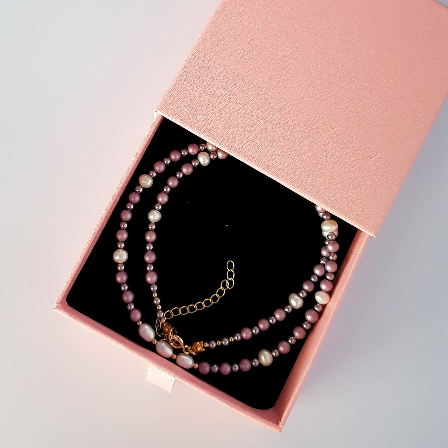 Pearl necklace with gold chain in a pink jewelry box on a light gray background