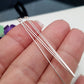A pair of flat head headpins made of sterling silver, held in a person's fingers, with a blurred background.