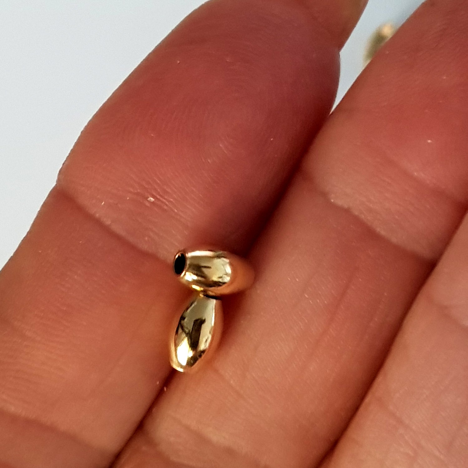 Gold oval-shaped beads on a finger against a neutral background