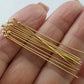 Gold headpins laying on a persons hand on a white background