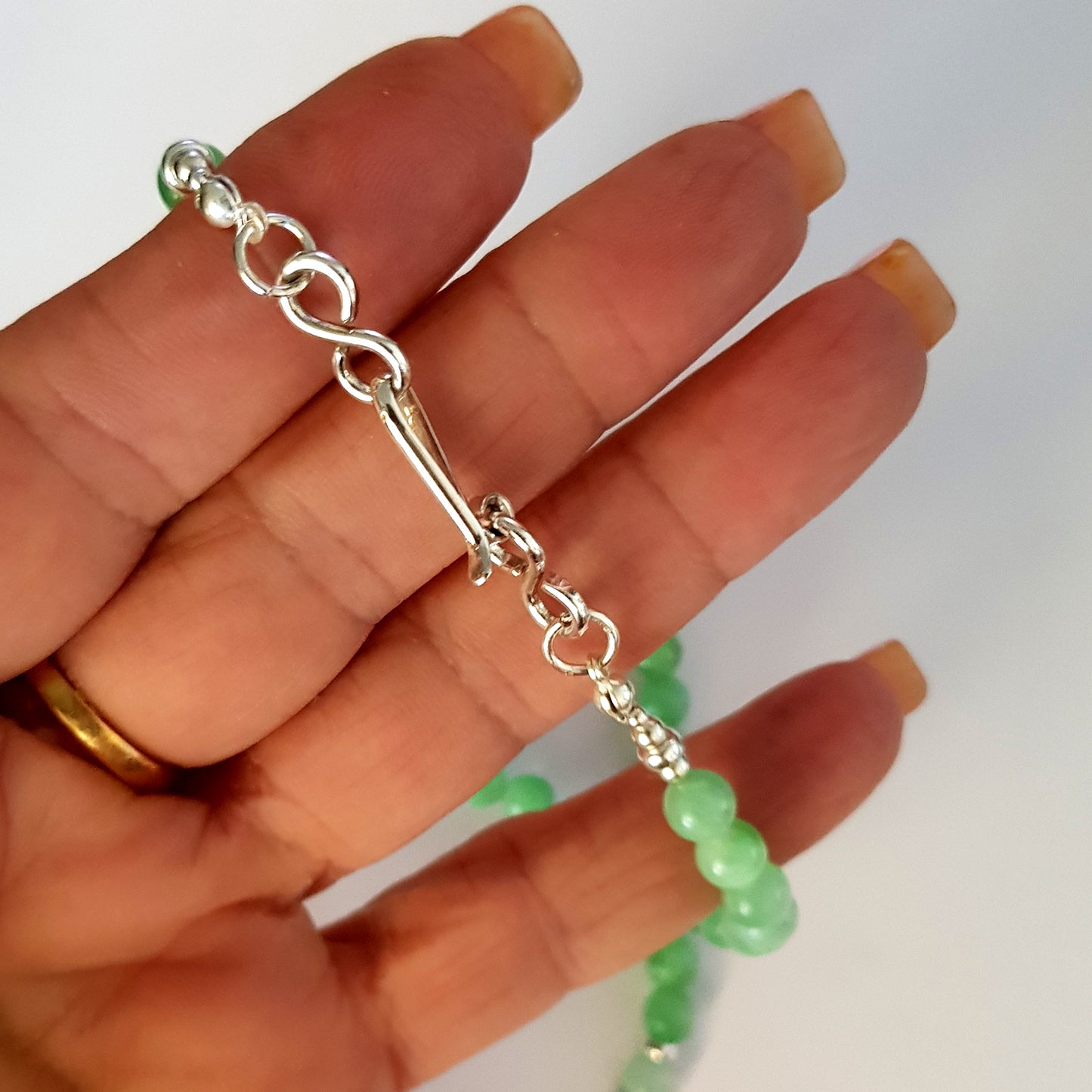 Silver chain Handmade clasp with green beads on a hand against a white background