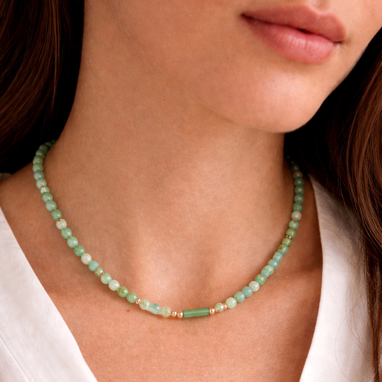Close-up of a woman wearing a green beaded necklace against a neutral background