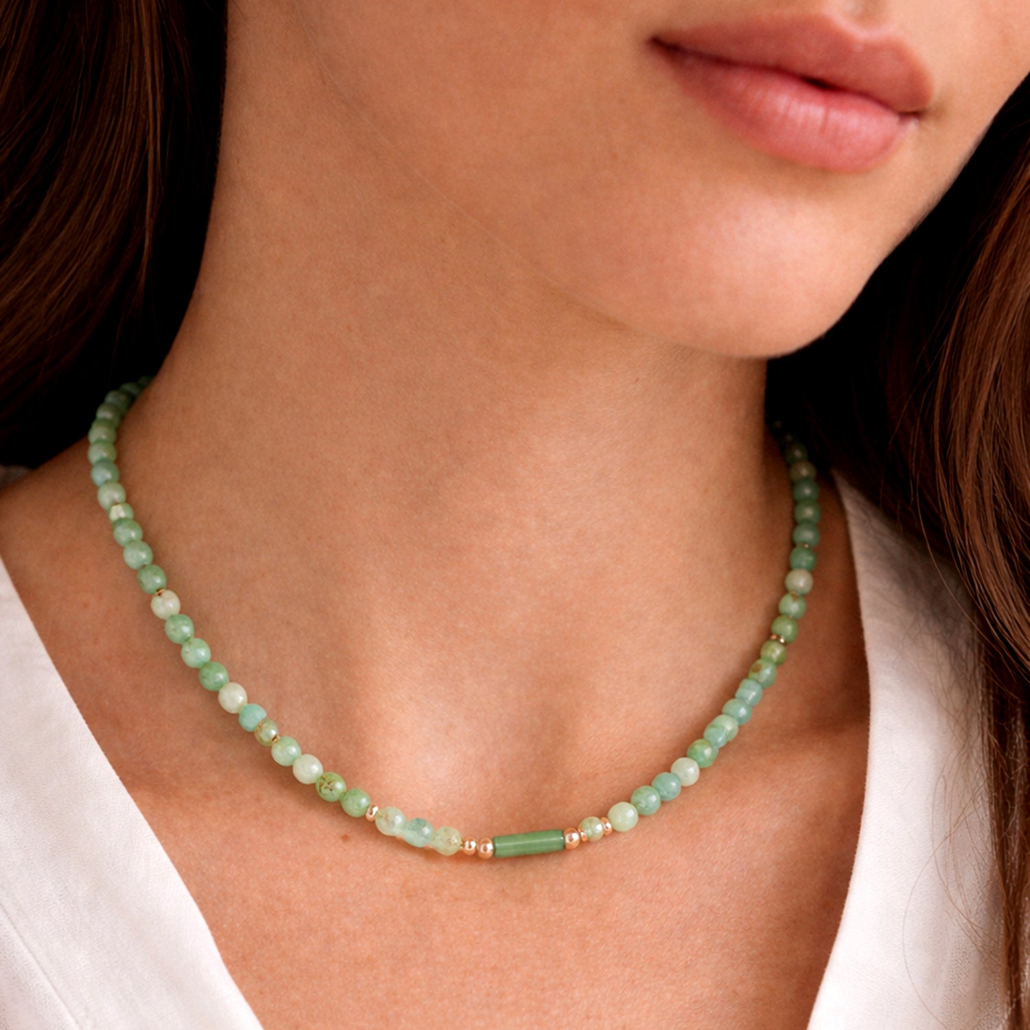 Close-up of a woman wearing a green beaded necklace against a neutral background