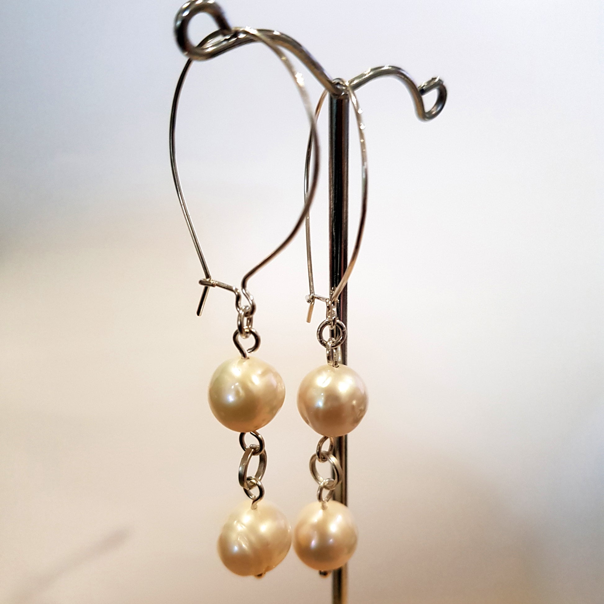Handmade sterling silver kidney hook earrings with two white freshwater pearls displayed on an earring stand – FKJ-209E by Kalitheo