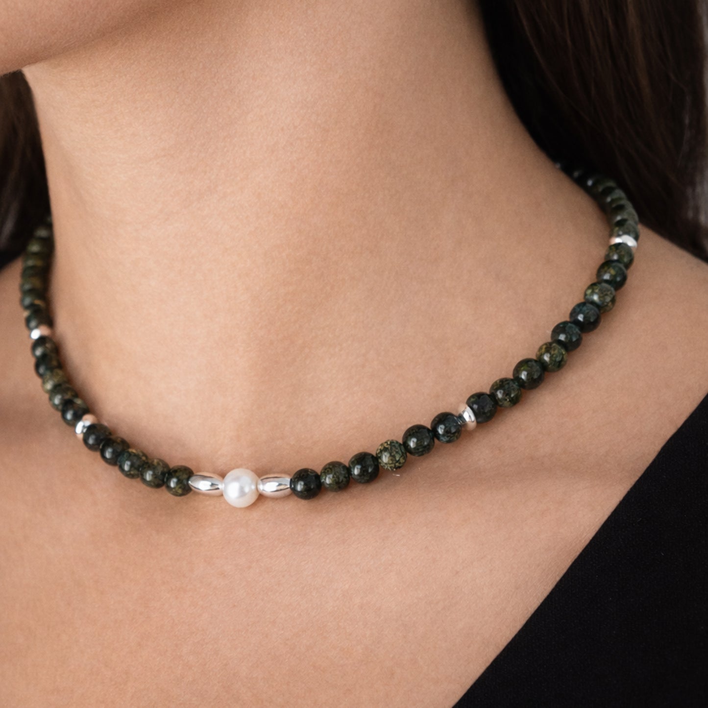 Necklace with green beads and a pearl on a person's neck
