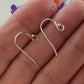A pair of sterling silver earring hooks with balled ends, displayed on a person's finger.