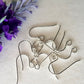 A bunch of silver hooks laying flat on white background, purple flower top corner.