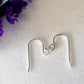 A pair of silver hooks laying flat on a white background, purple flower top corner
