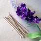 a bunch on silver eye pins laying flat on a white background next to a purple flower.