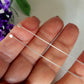 A pair of ball flat headpins laid on a human finger, showing their length and shape used for jewelry making.