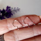 A pair of small kidney-shaped silver earring hooks held between fingers, with a polished and shiny finish.