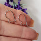 A pair of small kidney-shaped silver earring hooks held between fingers, with a polished and shiny finish.