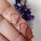 A pair of small kidney-shaped silver earring hooks held between fingers, with a polished and shiny finish.