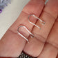 A pair of polished silver open kidney earring hooks held in a person's hand.
