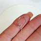 Silver earring with a small charm held between fingers on a light background