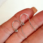 Silver earrings held between fingers on a neutral background