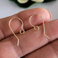 Gold earring hooks on a person's hand with a blurred background