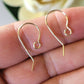 Gold earring hooks on a person's finger with a blurred background