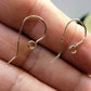 Gold earring hooks held between fingers on a neutral background